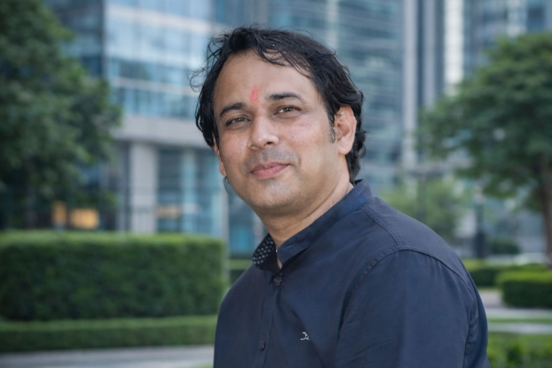 Professional close-up portrait of Vineet Kumar, Director of Atulya Computer Institute in Gaya, wearing an orange plaid shirt and glasses, with a subtle glowing orange halo against a dark-mode background. Identity preserved from source photo.
