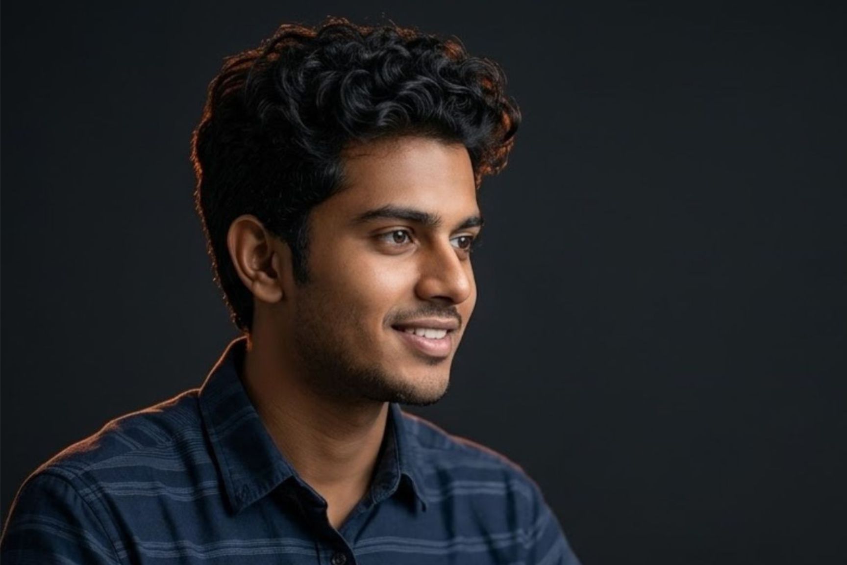 Professional close-up portrait of the exact student in the blue shirt from the source photo, smiling warm expression against a clean deep charcoal grey background with a subtle vibrant orange edge light, in a premium dark mode setting for Atulya Computer Institute in Gaya.